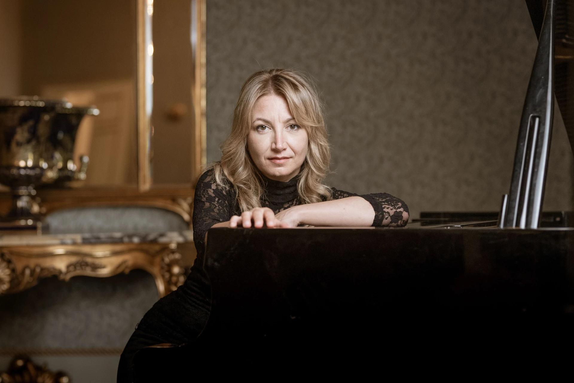Ilaria Sinicropi leaning on the grand piano, in a black lace dress