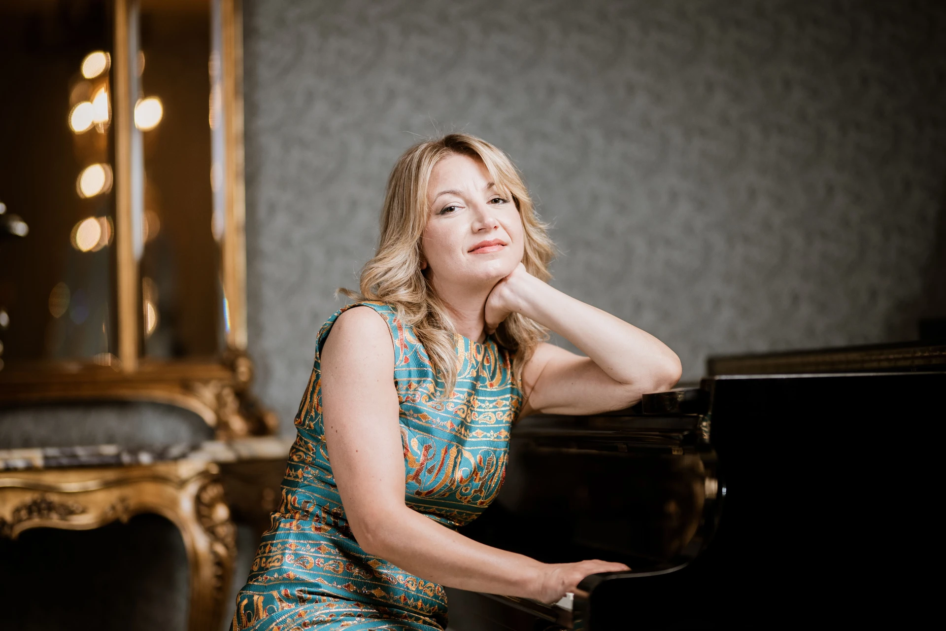 Ilaria Sinicropi smiling, leaning on the piano, in a turquoise dress